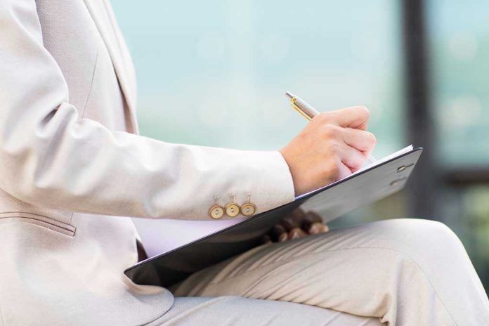 Person in beige suit writing on a clipboard
