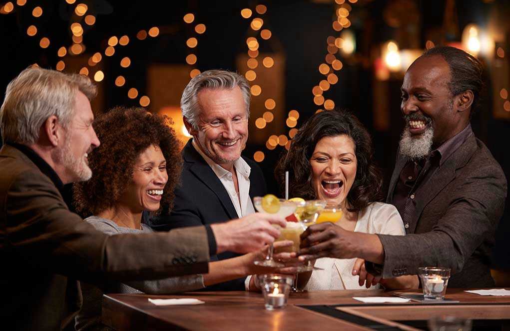People laughing while clinking glasses at a bar