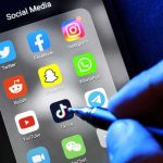 Social media apps on phone screen with hand holding stylus
