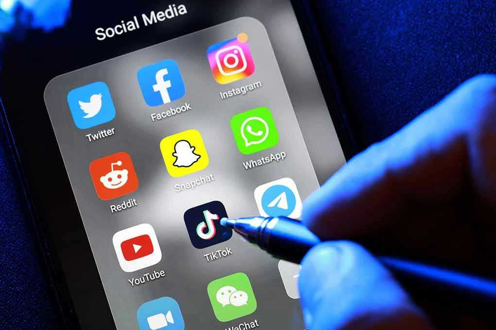 Social media apps on phone screen with hand holding stylus