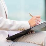 Person in beige suit writing on a clipboard