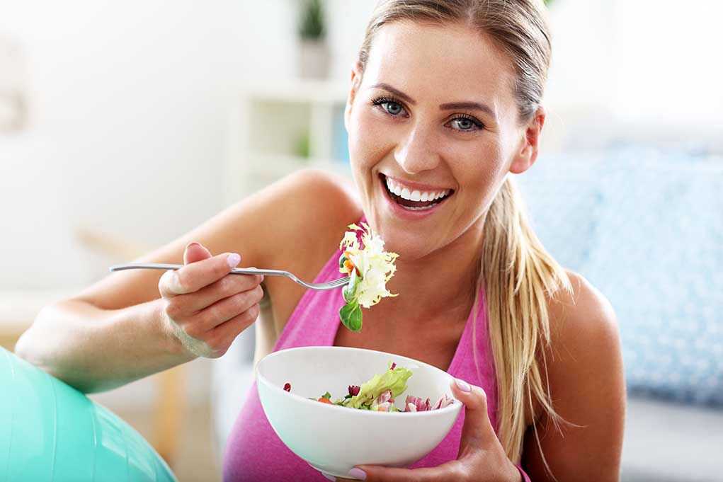 Woman smiling and eating a salad bowl