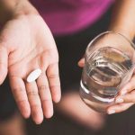 Person holding pill and glass of water