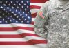 SHOCKING Army Restructure — Bureaucrats BYPASSED Soldier in camouflage uniform standing before American flag.