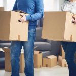 Two people carrying cardboard boxes indoors