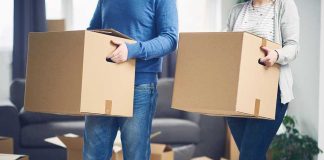 Two people carrying cardboard boxes indoors