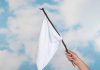 Hand holding white flag against a blue sky