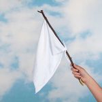 Hand holding white flag against a blue sky