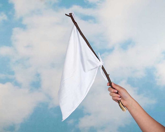 84861409 Hand holding white flag against a blue sky