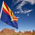 Arizona state flag waving in front of Monument Valley under a blue sky