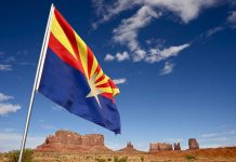 Arizona state flag waving in front of Monument Valley under a blue sky