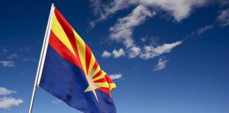 Arizona state flag waving in front of Monument Valley under a blue sky