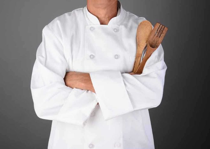 shutterstock_158666291.jpg A chef in a white uniform holding wooden cooking utensils with crossed arms