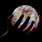 A hand holding a colorful crystal ball against a dark background