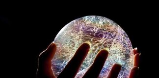A hand holding a colorful crystal ball against a dark background
