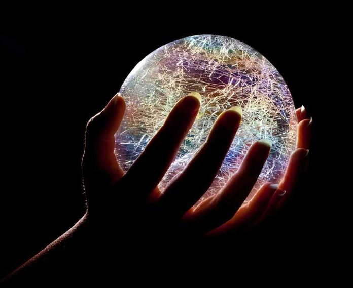 A hand holding a colorful crystal ball against a dark background