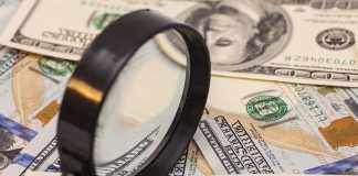 A magnifying glass resting on a pile of U.S. dollar bills
