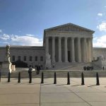 Supreme Court building with flag and people outside.