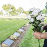 Person holding white roses at a cemetery.