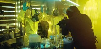armed officer confronts people in hazmat suits inside a lab