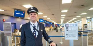 Airline pilot standing in airport check-in area with rolling bag