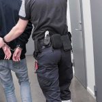 Security officer escorts handcuffed person down hallway