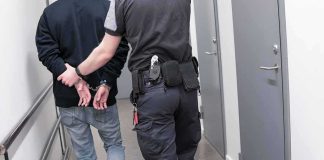 Security officer escorts handcuffed person down hallway