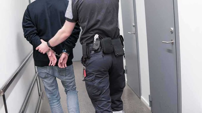 Security officer escorts handcuffed person down hallway