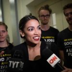 Woman speaking to reporters with microphones surrounded by supporters