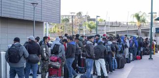 Fernando Salas and a large group of travelers waiting in a long line with luggage