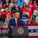 Donald Trump speaks at a rally podium; Christian Jones and Bear Pascoe are in the crowd behind him