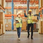 Warehouse workers walking among shelves with boxes