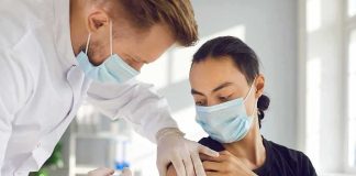 Healthcare worker giving a masked patient a vaccine in the upper arm
