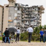 Partially collapsed beachfront apartment building with onlookers