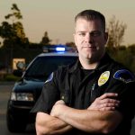 Police officer standing with arms crossed in front of patrol car