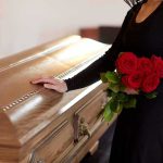 woman in black holding red roses beside a wooden casket