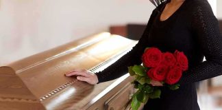 woman in black holding red roses beside a wooden casket