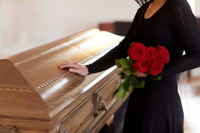 woman in black holding red roses beside a wooden casket